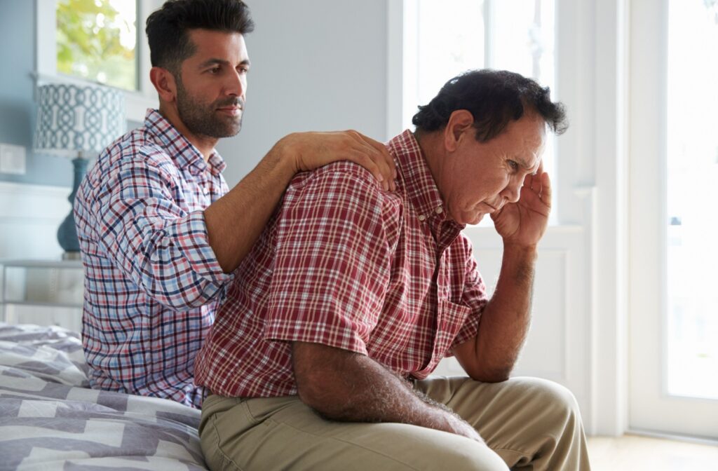 A concerned family member offers comfort to an elderly individual sitting on a bed