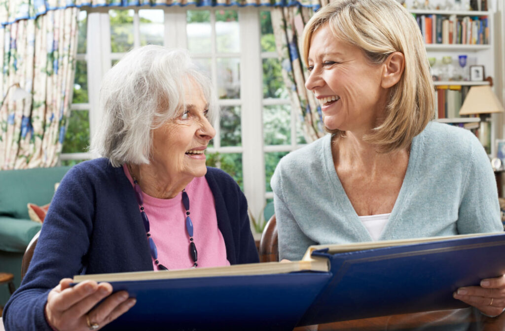 An adult child laughs while flipping through a photo album with their older parent during a visit in memory care