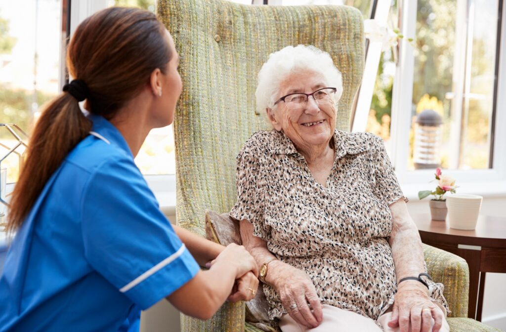 A caregiver checks in on a grinning resident in the lounge of a memory care community