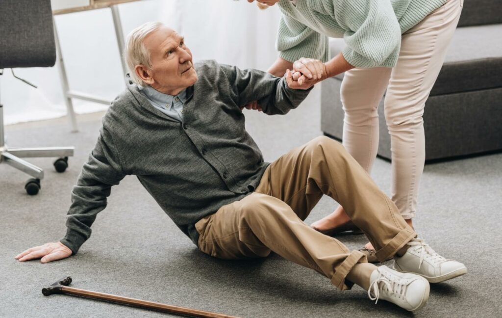 An adult offers a senior help standing after a fall.