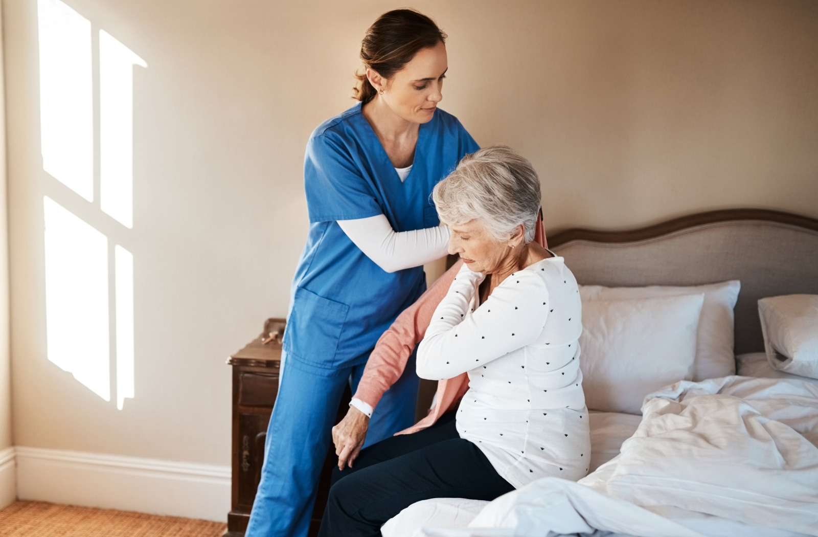 A caregiver assists a senior resident with putting on a sweater